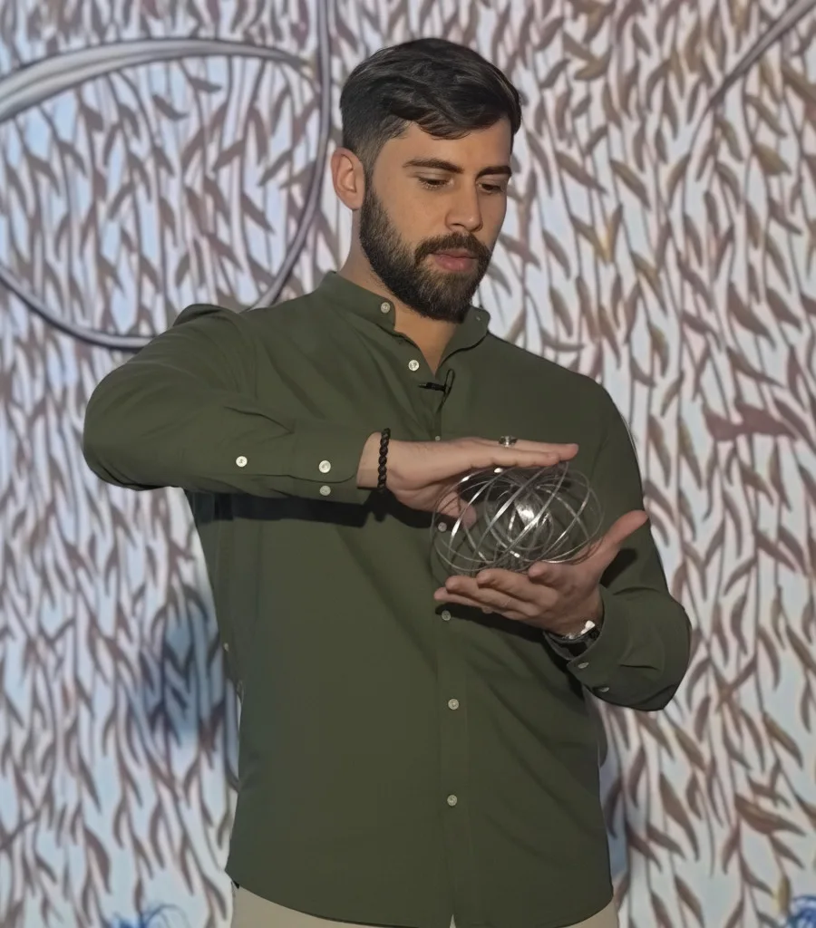 Tiago Braga, de camisa verde, segurando um anel de fluxo toroidal diante de uma projeção de padrões geométricos